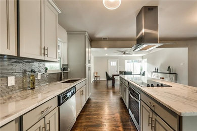 Mid-sized transitional galley medium tone wood floor and brown floor eat-in kitchen photo in Dallas with an undermount sink, raised-panel cabinets, quartzite countertops, gray backsplash, glass tile backsplash, stainless steel appliances and an island