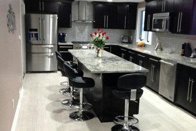 Example of a large trendy l-shaped porcelain tile enclosed kitchen design in New York with an undermount sink, recessed-panel cabinets, dark wood cabinets, granite countertops, gray backsplash, stone tile backsplash, stainless steel appliances and an island