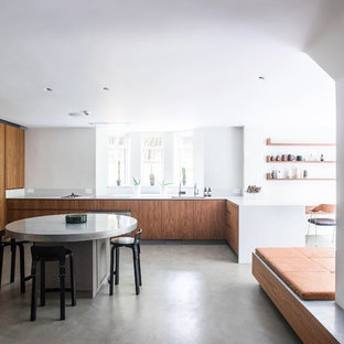 Large contemporary u-shaped open plan kitchen in London with a submerged sink, flat-panel cabinets, quartz worktops, white splashback, stainless steel appliances, concrete flooring, an island, grey floors, white worktops and medium wood cabinets.