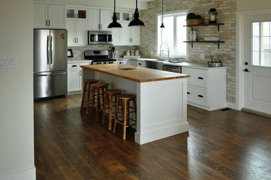 Inspiration for a mid-sized contemporary l-shaped dark wood floor eat-in kitchen remodel in Other with stainless steel appliances, an island, a farmhouse sink, shaker cabinets, white cabinets, wood countertops and beige backsplash