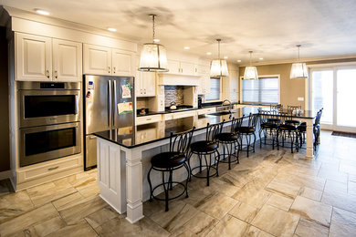 Example of a large transitional l-shaped ceramic tile and white floor open concept kitchen design in Other with an undermount sink, raised-panel cabinets, white cabinets, quartz countertops, gray backsplash, matchstick tile backsplash, stainless steel appliances and an island