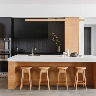 Design ideas for a contemporary galley kitchen in Other with an undermount sink, flat-panel cabinets, black cabinets, black splashback, stainless steel appliances, with island, grey floor and white benchtop.