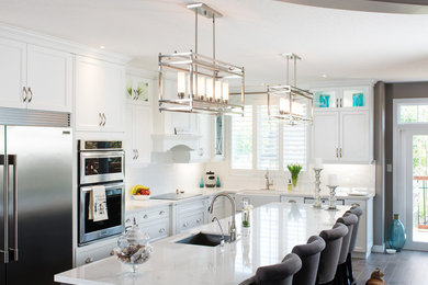 Inspiration for a large transitional l-shaped medium tone wood floor eat-in kitchen remodel in Toronto with a farmhouse sink, recessed-panel cabinets, white cabinets, quartz countertops, white backsplash, ceramic backsplash, stainless steel appliances and an island