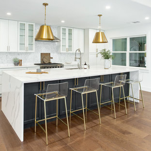 This is an example of a large contemporary galley open plan kitchen in Dallas with an undermount sink, shaker cabinets, white cabinets, quartz benchtops, white splashback, marble splashback, stainless steel appliances, medium hardwood floors, with island, brown floor and white benchtop.