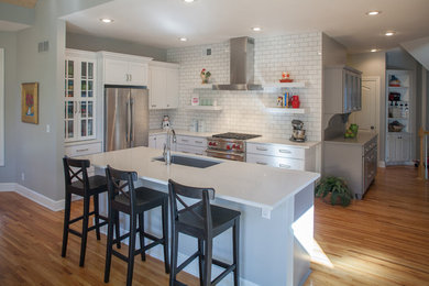 Eat-in kitchen - large transitional l-shaped medium tone wood floor and brown floor eat-in kitchen idea in Kansas City with an undermount sink, recessed-panel cabinets, white cabinets, quartz countertops, white backsplash, ceramic backsplash, stainless steel appliances and an island