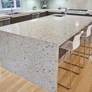 Inspiration for a mid-sized contemporary l-shaped eat-in kitchen in San Francisco with flat-panel cabinets, porcelain splashback, stainless steel appliances, light hardwood floors, a drop-in sink, dark wood cabinets, grey splashback, with island and recycled glass benchtops.