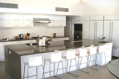 Example of a huge minimalist l-shaped open concept kitchen design in Los Angeles with flat-panel cabinets, white cabinets, white backsplash, paneled appliances and an island