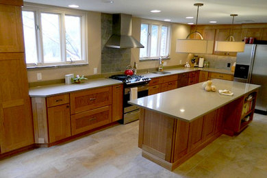 Example of a minimalist l-shaped ceramic tile eat-in kitchen design in Philadelphia with an undermount sink, recessed-panel cabinets, medium tone wood cabinets, granite countertops, beige backsplash, stone slab backsplash, stainless steel appliances and an island