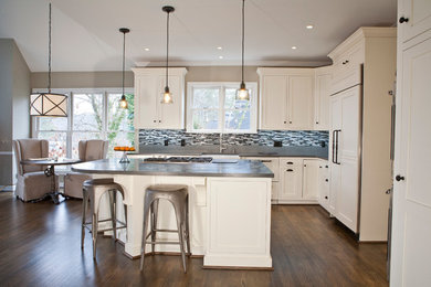 Large transitional l-shaped medium tone wood floor and brown floor eat-in kitchen photo in Atlanta with a farmhouse sink, shaker cabinets, white cabinets, solid surface countertops, multicolored backsplash, glass sheet backsplash, paneled appliances and an island