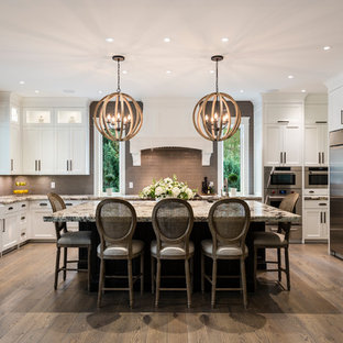 Foto di una cucina chic con lavello stile country, ante bianche, top in granito, paraspruzzi grigio, paraspruzzi in gres porcellanato, elettrodomestici in acciaio inossidabile, isola, pavimento marrone, ante in stile shaker e parquet scuro