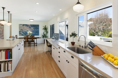 Mid-sized elegant l-shaped light wood floor enclosed kitchen photo in San Francisco with an undermount sink, shaker cabinets, white cabinets, white backsplash, subway tile backsplash, stainless steel appliances and an island