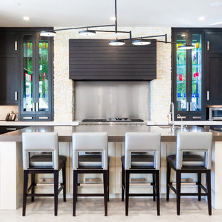 Ejemplo de cocina en L, tradicional renovada, con fregadero bajoencimera, armarios estilo shaker, puertas de armario negras, salpicadero metalizado, electrodomésticos de acero inoxidable, una isla, suelo beige y encimeras beige