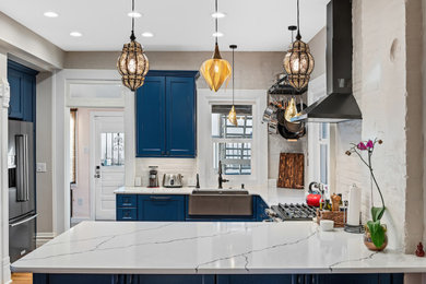 Example of a mid-sized eclectic u-shaped medium tone wood floor and brown floor eat-in kitchen design in Other with a farmhouse sink, recessed-panel cabinets, blue cabinets, quartz countertops, gray backsplash, brick backsplash, colored appliances, a peninsula and white countertops