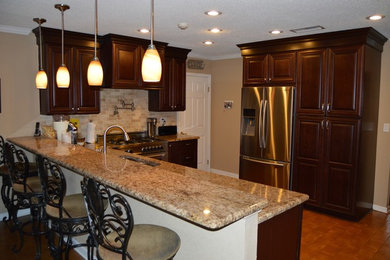 Mid-sized elegant l-shaped eat-in kitchen photo in New Orleans with an undermount sink, medium tone wood cabinets, granite countertops, beige backsplash, stone tile backsplash and stainless steel appliances