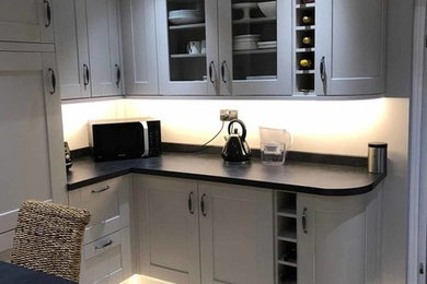 This is an example of a contemporary kitchen/diner in London with glass-front cabinets, grey cabinets, light hardwood flooring and black worktops.