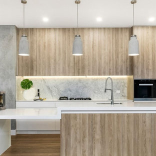 Photo of a contemporary kitchen in Melbourne with an undermount sink, flat-panel cabinets, light wood cabinets, grey splashback, marble splashback, black appliances, light hardwood floors, with island, beige floor and white benchtop.