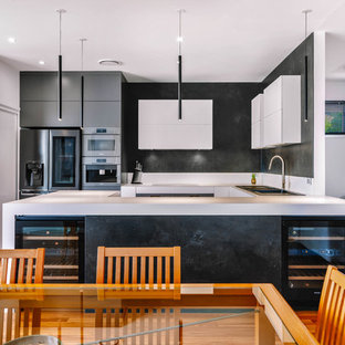 Inspiration for a contemporary u-shaped kitchen in Sunshine Coast with a drop-in sink, black appliances, medium hardwood floors, white benchtop, white cabinets, white splashback, porcelain splashback and with island.