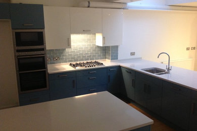 Example of a mid-sized trendy l-shaped light wood floor eat-in kitchen design in Hertfordshire with a drop-in sink, flat-panel cabinets, blue cabinets, blue backsplash, subway tile backsplash, paneled appliances and an island