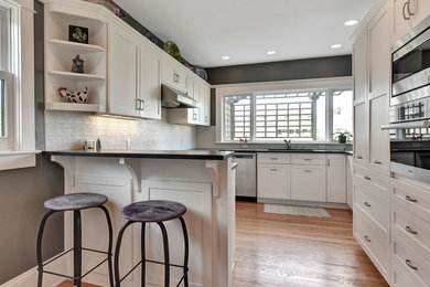 Mid-sized transitional u-shaped medium tone wood floor and brown floor eat-in kitchen photo in Portland with an undermount sink, shaker cabinets, white cabinets, soapstone countertops, white backsplash, glass tile backsplash, stainless steel appliances and a peninsula