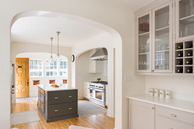 Example of a classic light wood floor and brown floor kitchen design in Portland with glass-front cabinets, gray cabinets, marble countertops, white backsplash, stone slab backsplash, stainless steel appliances, an island and white countertops