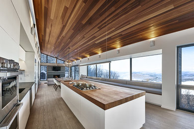 Inspiration for a large modern galley light wood floor and gray floor open concept kitchen remodel in Montreal with an undermount sink, flat-panel cabinets, white cabinets, wood countertops, white backsplash, stainless steel appliances, an island and window backsplash