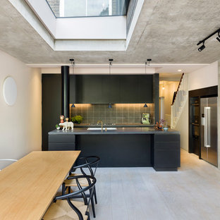 This is an example of a large industrial galley eat-in kitchen in London with an integrated sink, flat-panel cabinets, black cabinets, grey splashback, cement tile splashback, stainless steel appliances, light hardwood floors, with island, white floor and grey benchtop.