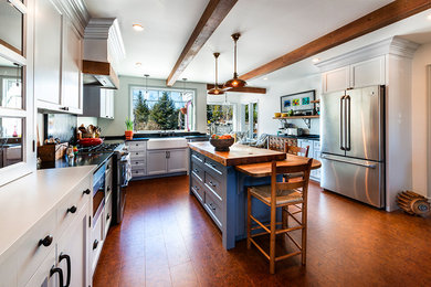 Large midcentury u-shaped open plan kitchen in Other with a belfast sink, shaker cabinets, white cabinets, composite countertops, stainless steel appliances, porcelain flooring, an island and brown floors.