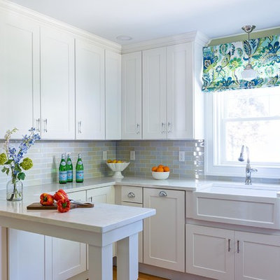 Inspiration for a small transitional u-shaped medium tone wood floor and brown floor kitchen remodel in Boston with a farmhouse sink, stainless steel appliances, white countertops, shaker cabinets, white cabinets, multicolored backsplash, subway tile backsplash and a peninsula