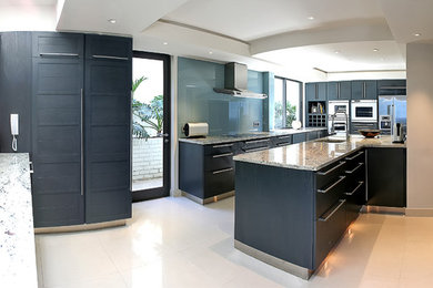Modelo de cocina contemporánea con armarios estilo shaker, puertas de armario azules, encimera de granito, salpicadero verde, salpicadero de vidrio templado y electrodomésticos de acero inoxidable