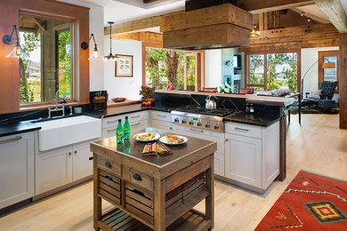 Example of a mountain style light wood floor open concept kitchen design in Other with a farmhouse sink, shaker cabinets, white cabinets, stainless steel appliances and an island
