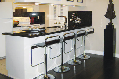 Mid-sized transitional galley dark wood floor and brown floor kitchen photo in Toronto with an undermount sink, raised-panel cabinets, white cabinets, granite countertops, white appliances and a peninsula