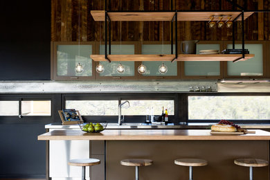 Diseño de cocina comedor lineal industrial de tamaño medio con encimera de madera, salpicadero de vidrio y una isla