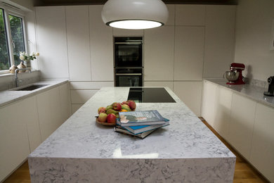 This is an example of a medium sized contemporary u-shaped open plan kitchen in London with a built-in sink, flat-panel cabinets, white cabinets, white splashback, integrated appliances and an island.
