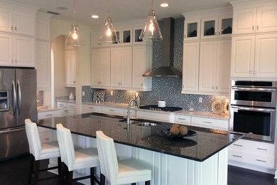 Example of a mid-sized minimalist l-shaped eat-in kitchen design in Other with an undermount sink, raised-panel cabinets, white cabinets, granite countertops, gray backsplash, glass tile backsplash, stainless steel appliances and an island