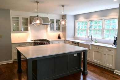 Inspiration for a large craftsman u-shaped medium tone wood floor and brown floor eat-in kitchen remodel in Philadelphia with a farmhouse sink, recessed-panel cabinets, white cabinets, marble countertops, white backsplash, ceramic backsplash, stainless steel appliances and an island