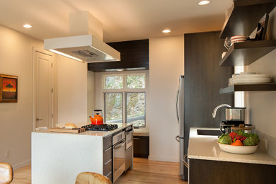 This is an example of a medium sized modern single-wall kitchen/diner in Other with flat-panel cabinets, dark wood cabinets, a submerged sink, soapstone worktops, stainless steel appliances, light hardwood flooring and an island.
