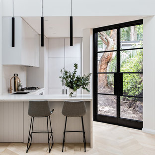 This is an example of a contemporary l-shaped kitchen in Sydney with an undermount sink, flat-panel cabinets, grey cabinets, white splashback, marble splashback, light hardwood floors, a peninsula, beige floor and white benchtop.