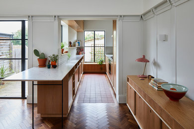 This is an example of a midcentury galley kitchen in London with flat-panel cabinets, medium wood cabinets, white splashback, a breakfast bar and white worktops.