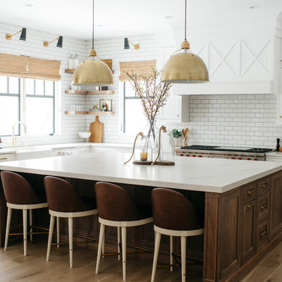 Farmhouse l-shaped medium tone wood floor and brown floor eat-in kitchen photo in Detroit with a farmhouse sink, shaker cabinets, white cabinets, white backsplash, subway tile backsplash, stainless steel appliances, an island and white countertops