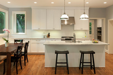 Elegant single-wall medium tone wood floor and brown floor eat-in kitchen photo in DC Metro with an undermount sink, recessed-panel cabinets, white cabinets, white backsplash, stainless steel appliances and an island