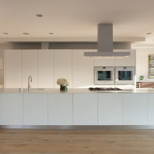 Inspiration pour une cuisine américaine parallèle minimaliste avec un évier intégré, un placard à porte plane, des portes de placard blanches, un électroménager blanc, un sol en bois clair et un îlot central.