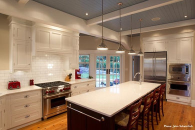 Diseño de cocina clásica renovada grande con electrodomésticos de acero inoxidable, suelo de madera clara, una isla, encimera de cuarcita, salpicadero blanco y salpicadero de azulejos tipo metro