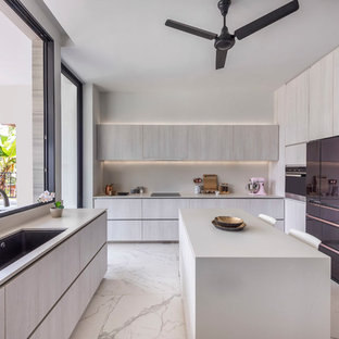 This is an example of a contemporary u-shaped separate kitchen in Singapore with an undermount sink, flat-panel cabinets, beige cabinets, white splashback, black appliances, with island, white floor and white benchtop.