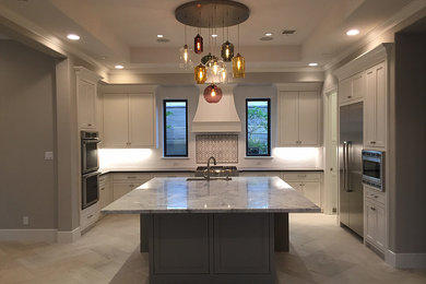 Mid-sized transitional l-shaped marble floor enclosed kitchen photo in Houston with an undermount sink, shaker cabinets, stainless steel cabinets, granite countertops, white backsplash, porcelain backsplash, stainless steel appliances and an island