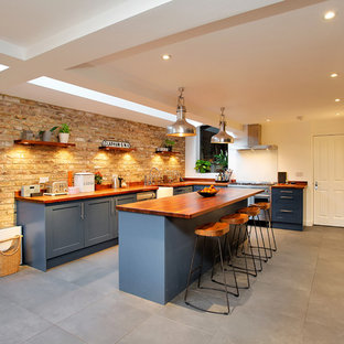 Inspiration for a large country l-shaped kitchen in London with a belfast sink, recessed-panel cabinets, blue cabinets, wood worktops, stainless steel appliances, an island, grey floors and brown worktops.