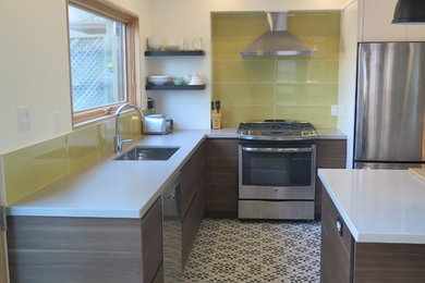 This is an example of a medium sized retro l-shaped kitchen/diner in Toronto with flat-panel cabinets, dark wood cabinets, engineered stone countertops, yellow splashback, glass tiled splashback, stainless steel appliances, ceramic flooring, an island, multi-coloured floors and a submerged sink.