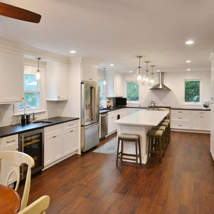 Photo of an expansive transitional u-shaped eat-in kitchen in Philadelphia with an undermount sink, recessed-panel cabinets, white cabinets, quartz benchtops, white splashback, subway tile splashback, stainless steel appliances, vinyl floors, with island, brown floor and white benchtop.