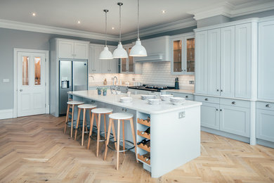 Inspiration for a large classic l-shaped open plan kitchen in Hertfordshire with shaker cabinets, blue cabinets, an island, a built-in sink, granite worktops, white splashback, ceramic splashback, stainless steel appliances, light hardwood flooring and beige floors.