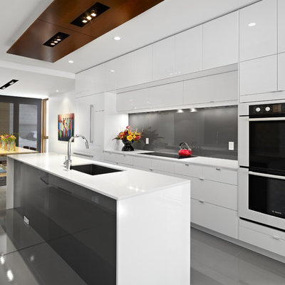 Inspiration for a contemporary galley eat-in kitchen remodel in Edmonton with a single-bowl sink, flat-panel cabinets, white cabinets, gray backsplash, glass sheet backsplash, paneled appliances and white countertops