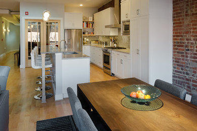 Example of a large l-shaped light wood floor open concept kitchen design in Detroit with white cabinets, gray backsplash, stainless steel appliances and an island